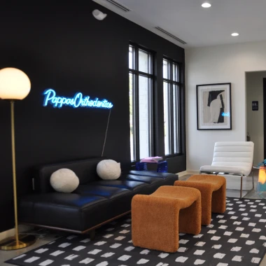 Modern lobby at Pappas Orthodontics with seating area, neon sign, artwork, and bright lighting.